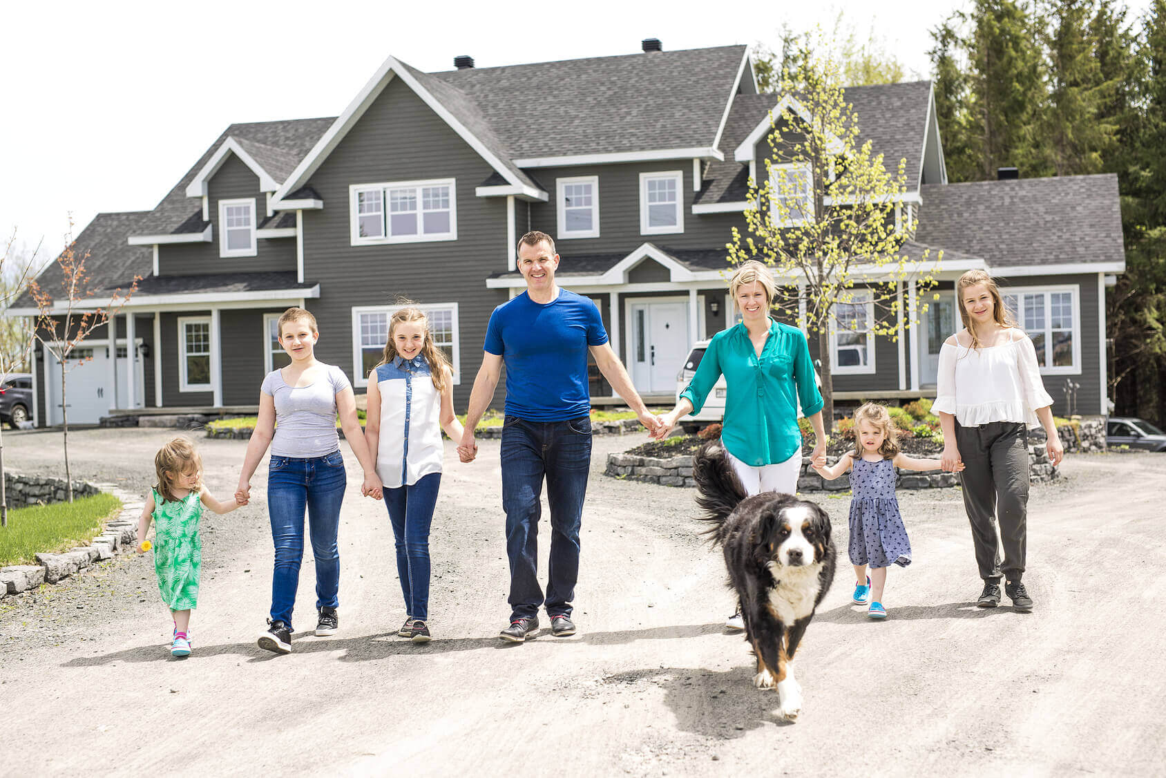 Immobilienbesitzer steht mit seiner Familie, vor eigenem Haus.